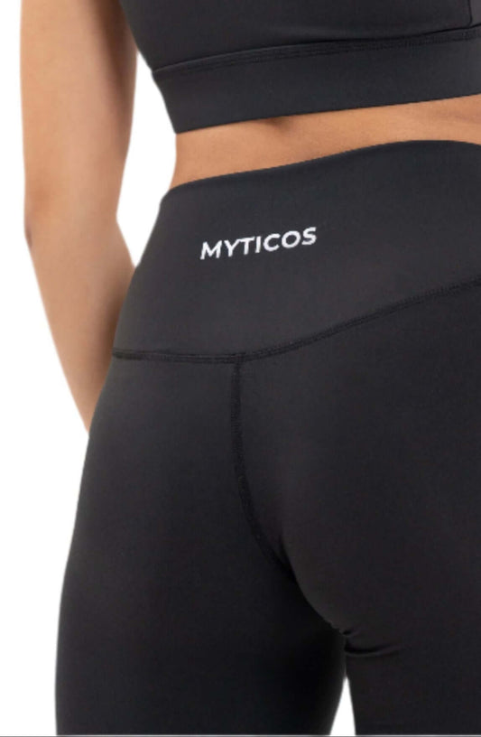 Back view of woman wearing Myticos®️ black sports bra and leggings set, highlighting the logo on the waistband and racerback design of the bra against a white background.