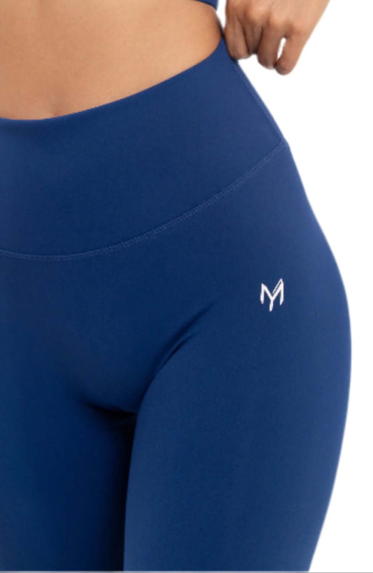 Woman adjusting Myticos®️ navy blue sports bra and leggings set, showcasing the fit and design details of the activewear against a white background.