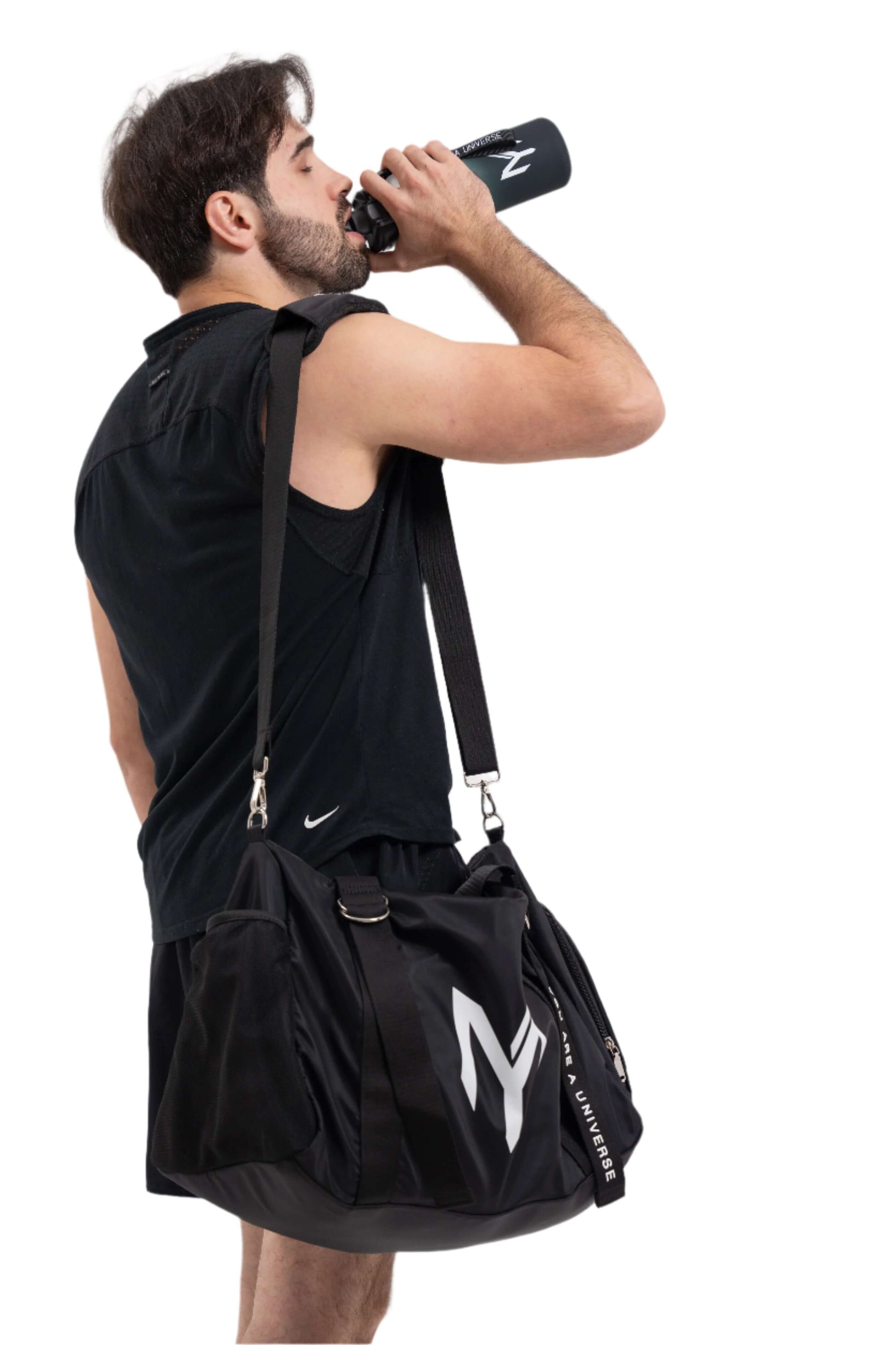 Man drinking from a water bottle with a black gym bag on his shoulder against a white background