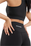 Close-up of Myticos®️ logo on black women's leggings waistband, highlighting stitching, fabric texture, and premium fit against a white background.