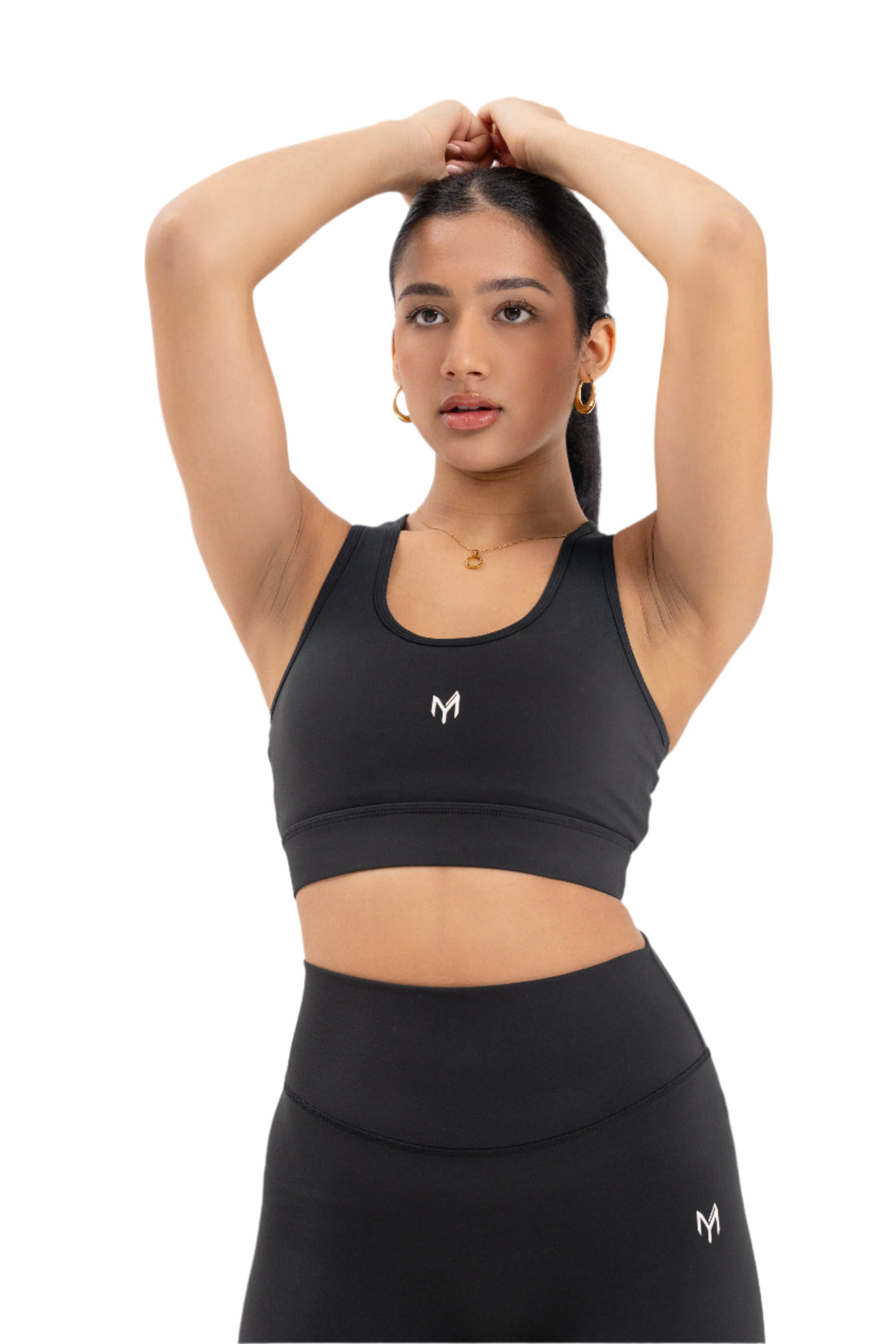 Close-up front view of woman wearing Myticos®️ black sports bra and leggings set, posing with arms raised to showcase the sleek fit and design against a white background.