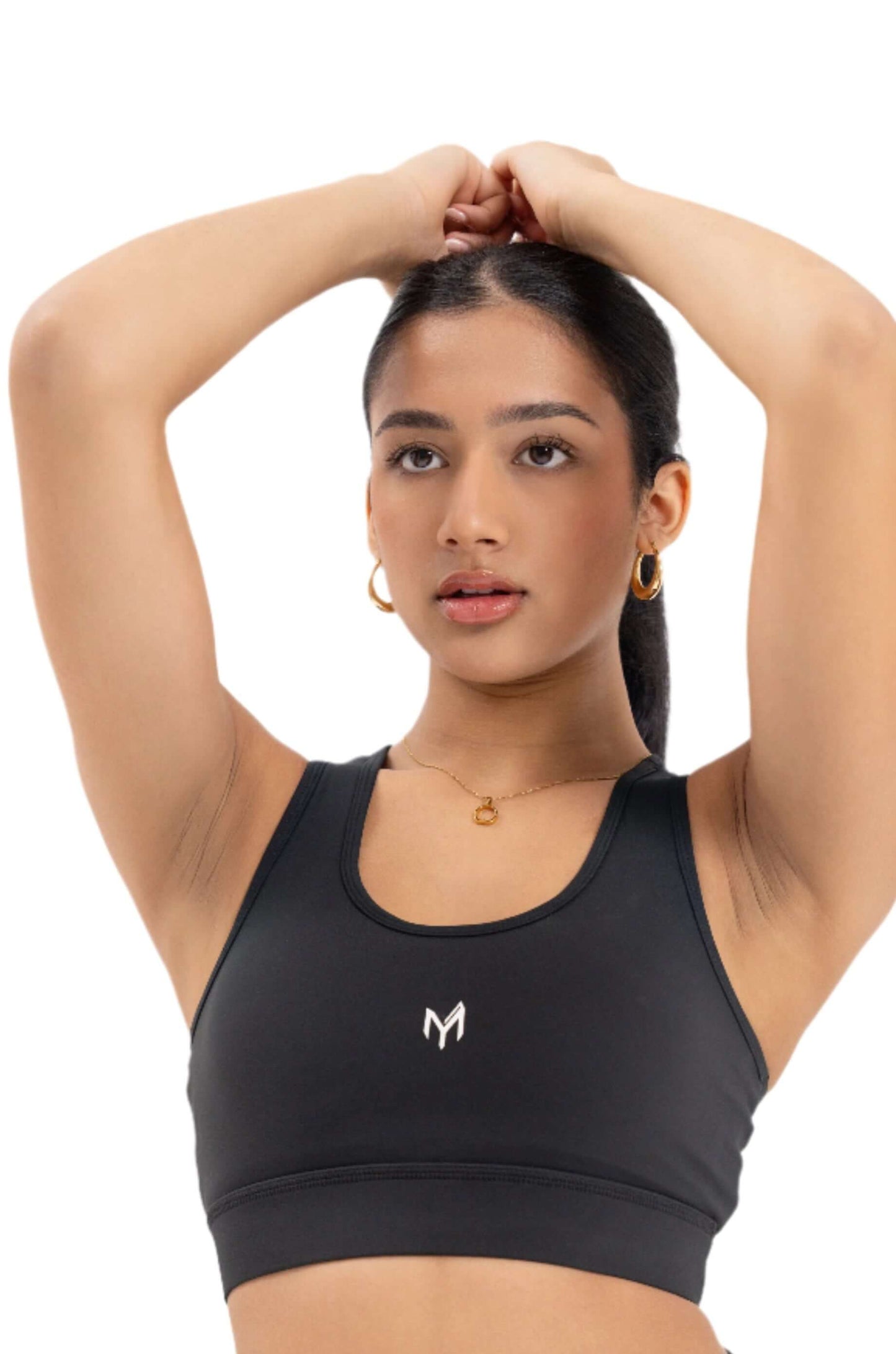 Close-up front view of woman wearing Myticos®️ black sports bra and leggings set, posing with arms raised to showcase the sleek fit and design against a white background.