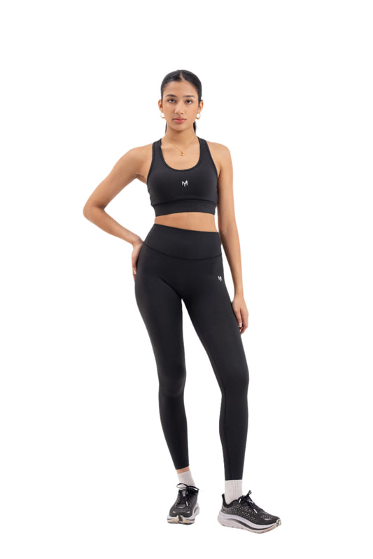 Front view of woman wearing Myticos®️ black sports bra and leggings set, designed for activewear with a sleek, supportive fit against a white background.