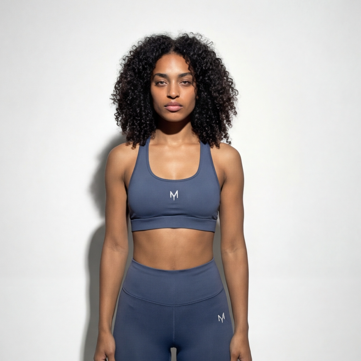 Woman wearing a blue sports bra and leggings with a logo on a white background