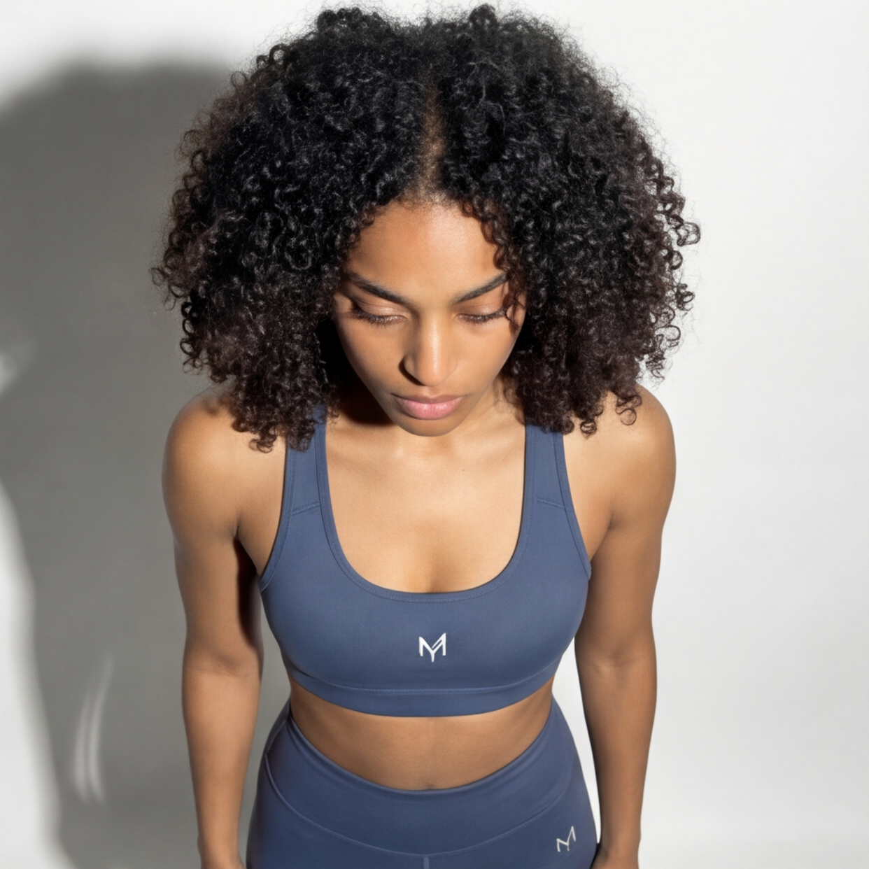 Woman wearing a blue sports bra and leggings with a logo on a white background