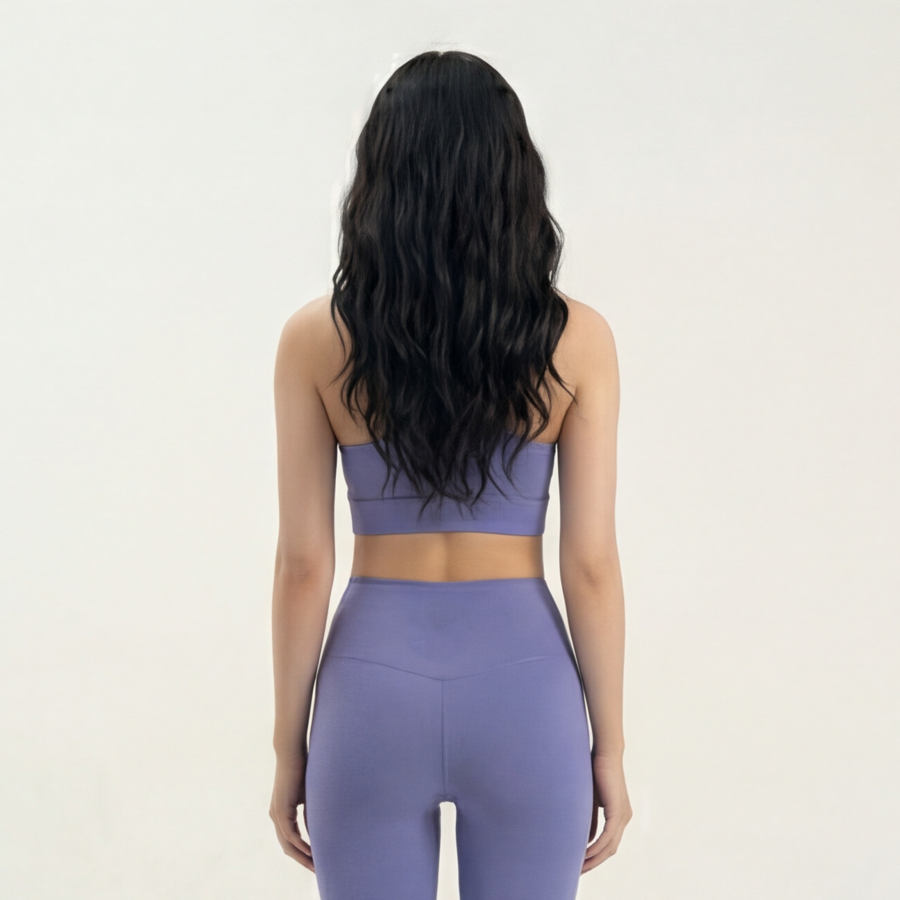 Person wearing a purple sports bra and leggings set on a plain background